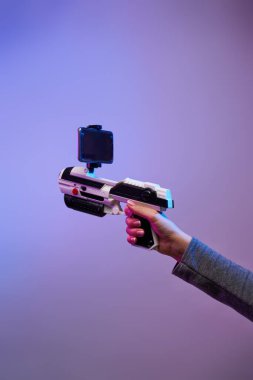 Eflatun bir arka planda artırılmış gerçeklik içeren oyunlar için bir silah taşıyan kadın elleri.