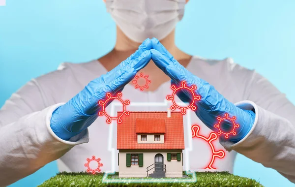 Žena v lékařských rukavicích a masce drží ruce nad domem. Koncept pobytu doma, karanténa, zabezpečení uvnitř domu. — Stock fotografie