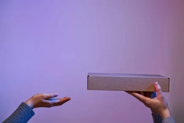 Duas mãos com caixa de papelão no fundo roxo em branco . — Fotografia de Stock