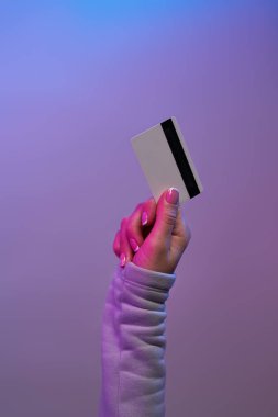 Mor arka planda el ele tutuşan kredi kartı.