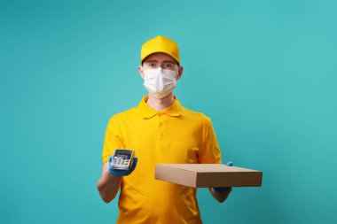 Yüzünde tıbbi maske olan kurye kutusunu ve iğnesini tutuyor..