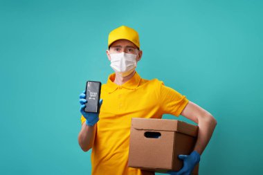 Yüzünde tıbbi maske olan kurye elinde telefon ve kutu tutuyor..