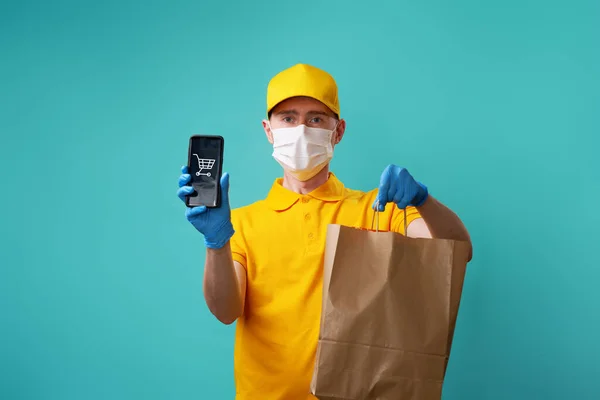 Mensajero con máscara médica en la cara sostiene la bolsa y el teléfono inteligente en la mano . —  Fotos de Stock