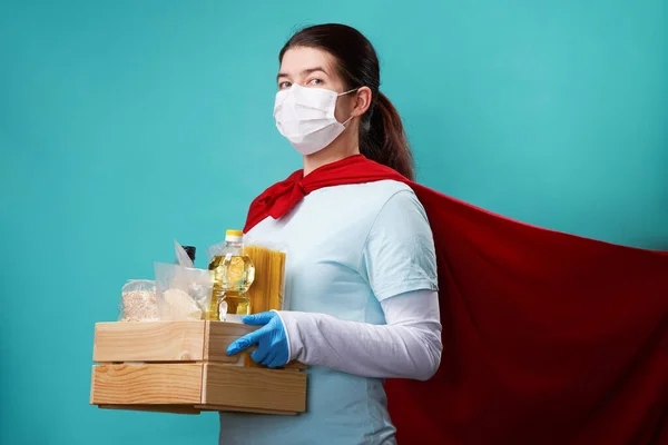 Dobrovolník na sobě chirurgické masky a superhrdina plášť drží jídlo box. — Stock fotografie