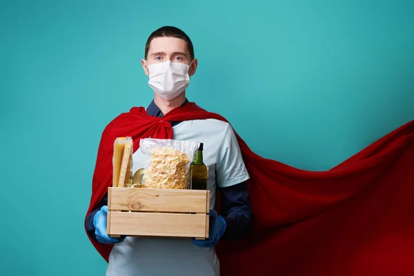 Volunteer wearing surgical mask and superhero cloak holds food box.