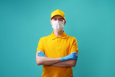 Kurye sarı tişört ve şapka giyiyor. Koruyucu tıbbi eldiven ve maske takıyor..