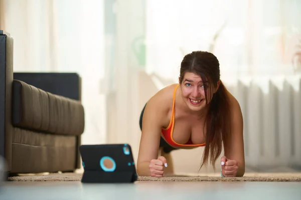 Femmes en vêtements d'entraînement athlétique fait un exercice de planche tout en utilisant des tutoriels vidéo . — Photo