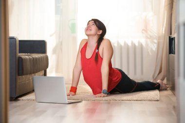 Kadın gerinme hareketleri yapıyor, video dersleri kullanarak evde yoga egzersizleri yapıyor..