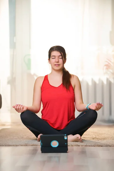 Mulher pratica ioga e medita na posição de lótus em casa usando tutoriais em vídeo . — Fotografia de Stock