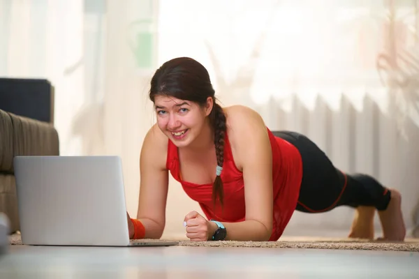 Frauen in sportlicher Trainingskleidung machen eine Brettübung, während sie Videotutorials nutzen. — Stockfoto