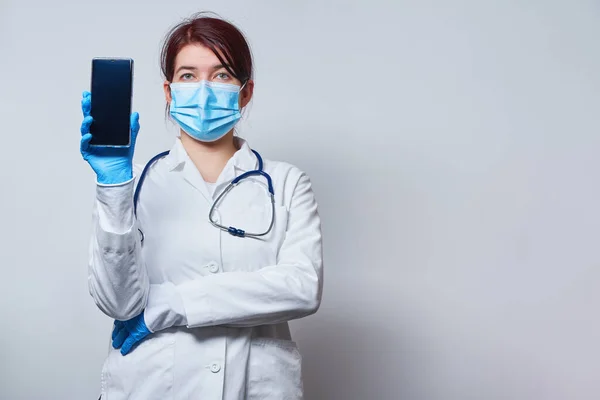 Cerrahi maskeli ve tıbbi eldivenli doktor elinde bir akıllı telefon tutuyor.. — Stok fotoğraf