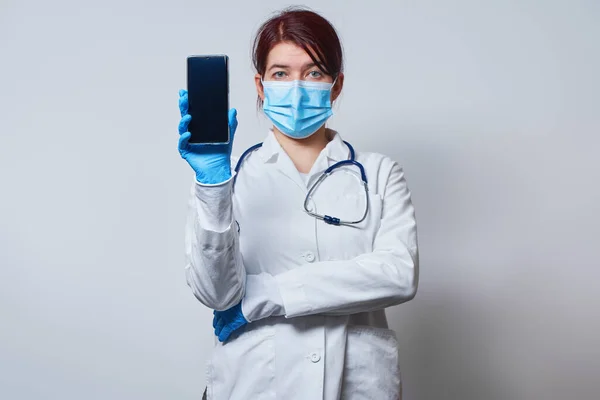 Доктор в хірургічній масці і медичні рукавички тримає в руці смартфон . — стокове фото