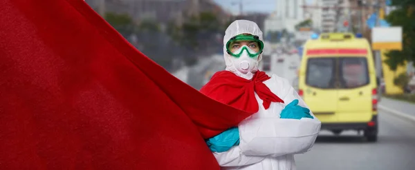 El médico está usando PPE - traje, guantes y mascarilla quirúrgica en capa de superhéroe contra el fondo de la ciudad . —  Fotos de Stock