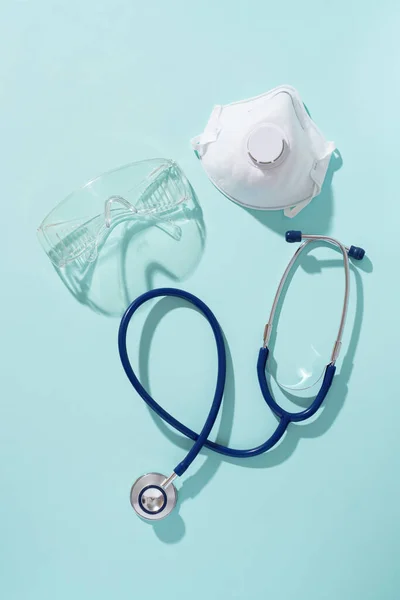 Phonendoskop, Atemschutzmaske und Schutzbrille auf blauem Hintergrund. — Stockfoto