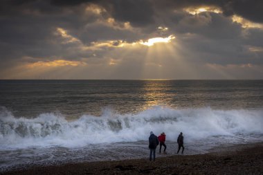 Güneş batarken Brighton sahilinde üç adam.