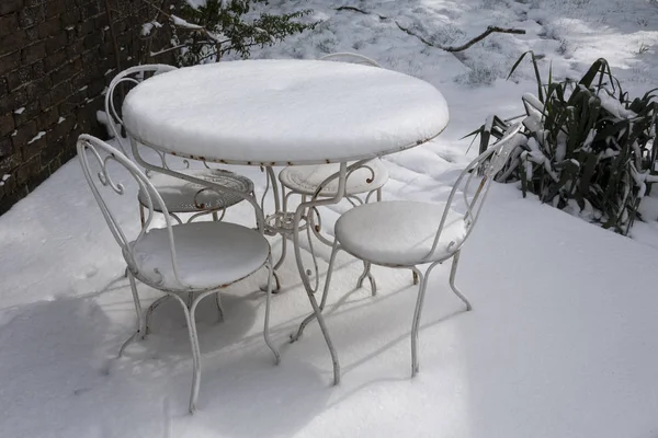 Masa ve sandalyeler kalın karla kaplı bahçede.