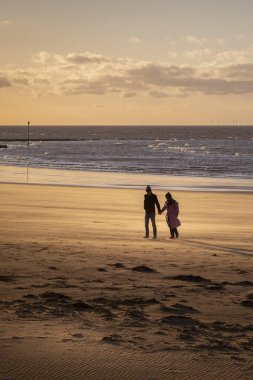 Gün batımında Margate sahilinde yürüyen çift.
