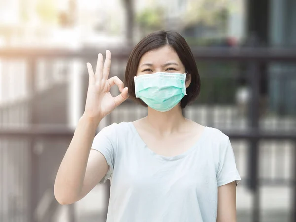 Asian woman wearing mask and ok finger hands gesture on blurred background with sunlight