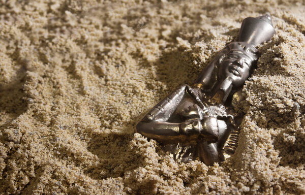 Pharaoh metal statuette laying in sand.