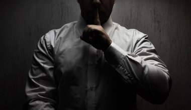 Bir korkunç korku adamın beyaz gömlek ayakta sessizlik el işaret gösteren siyah arka plan üzerine üst ışık altında fotoğraf.