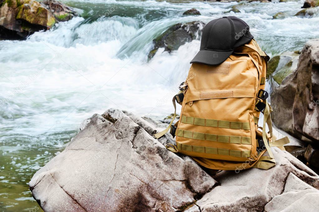 Travel backpack standing on forest river waterfall rock.