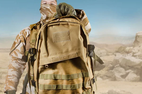 Soldado de uniforme segurando mochila no fundo do deserto . — Fotografia de Stock