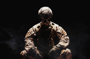Tam teçhizatlı bir çöl askerinin karanlık sisli arka planda oturan zırhlı, kasklı ve eldivenli fotoğrafı..