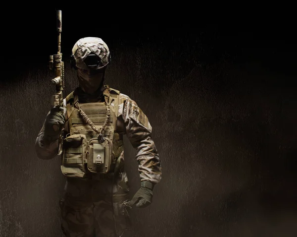 一个装备齐全的沙漠迷彩服士兵戴着面具 盔甲和手套 手持来复枪站在黑暗雾蒙蒙的混凝土前视镜下的照片 — 图库照片