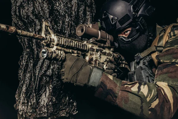 Foto Soldado Totalmente Equipado Uniforme Camuflagem Sentado Apontando Rifle Perto — Fotografia de Stock
