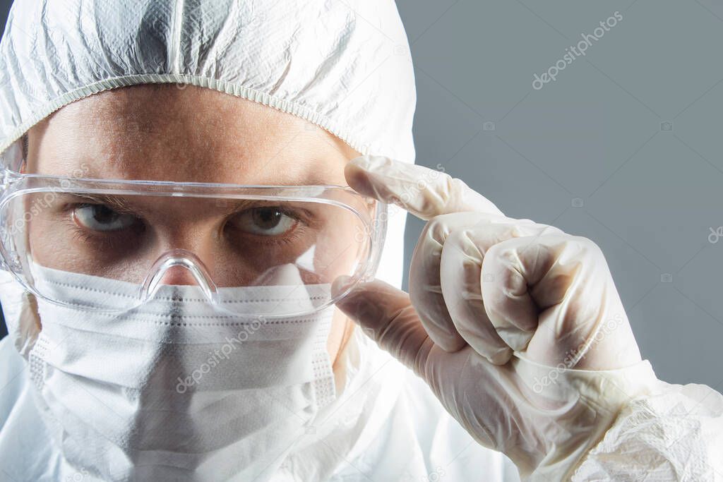 Portrait photo of medic in gloves. costume and mask holding protective glasses.