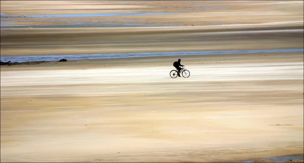 Cyclist on a wide flat beach at low tide taking exercise.