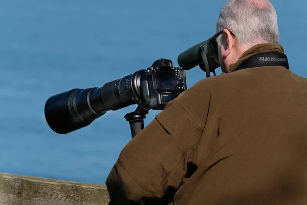 Man with camera and long telephoto lens on tripod.