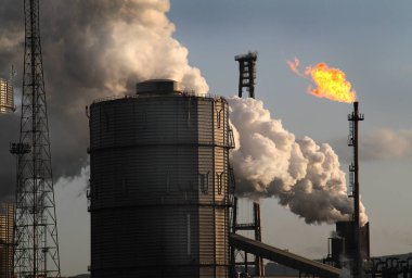 Large integrated steelworks site with gas holder, gas flare stack and large steam emission from a hot coke quench. clipart