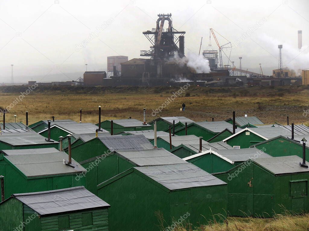Green fishermen's huts at Redcar in north Yorkshire with large industrial complex in the background.                               