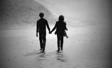 Dalgalar çekildiğinde ıslak bir sahilde el ele yürüyen çiftlerin silueti..