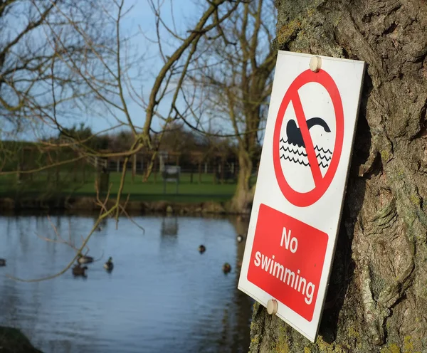 Safety sign banning any swimming on the bank of a duck pond on a holiday making complex.