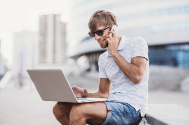 Akıllı telefonlu genç adam dizüstü bilgisayar kullanıyor. 