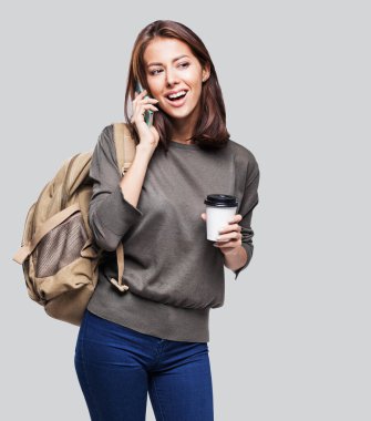 Sırt çantalı, elinde akıllı telefon ve kahve fincanı olan güzel bir kadın.