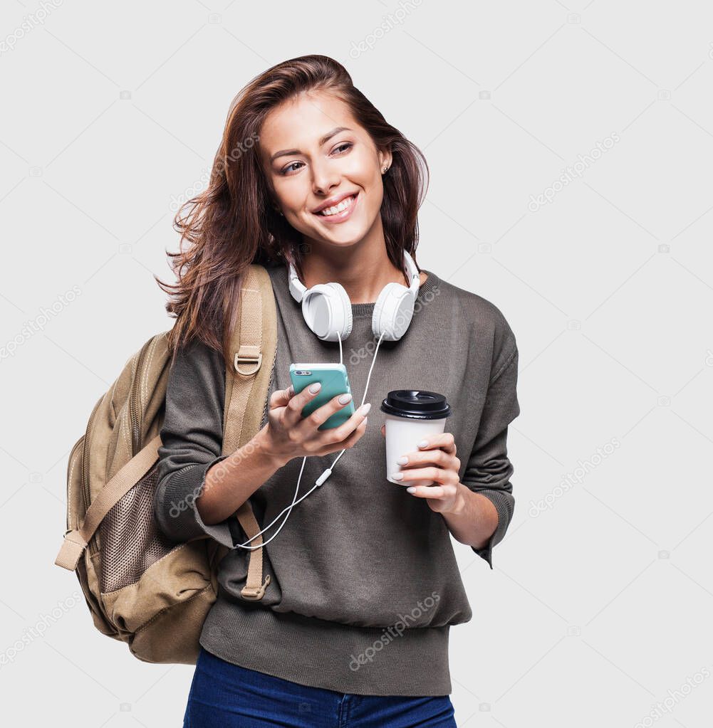 Young beautiful woman with backpack holding smartphone and coffee cup