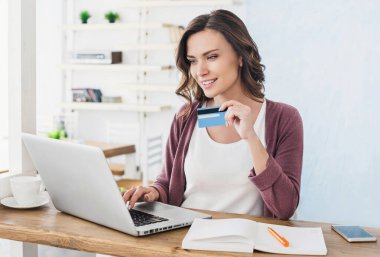 Genç ve güzel bir kadın evde bilgisayar ve alışveriş yapıyor.