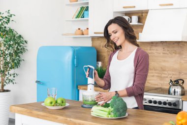 Genç ve güzel bir kadın yemek pişiriyor ve blender kullanıyor.