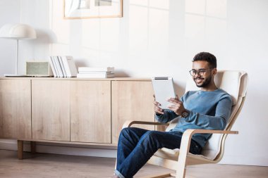 Evde dijital tablet kullanan yakışıklı bir genç, odasında dinlenen öğrenci, ev işi ya da öğrenimi, serbest çalışma, online alışveriş, uzaktan eğitim konsepti