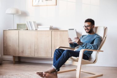 Evde dijital tablet kullanan yakışıklı bir genç, odasında dinlenen öğrenci, ev işi ya da öğrenimi, serbest çalışma, online alışveriş, uzaktan eğitim konsepti