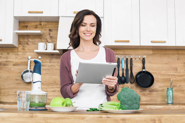 Young beautiful woman using tablet while cooking 