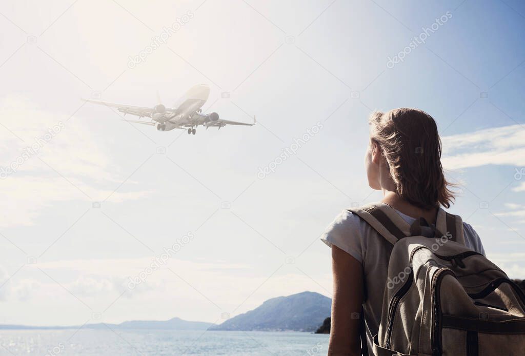 Young woman with backpack and airplane in sky, back side of traveler girl looking at flying plane above sea, travel, tourism and active lifestyle concept