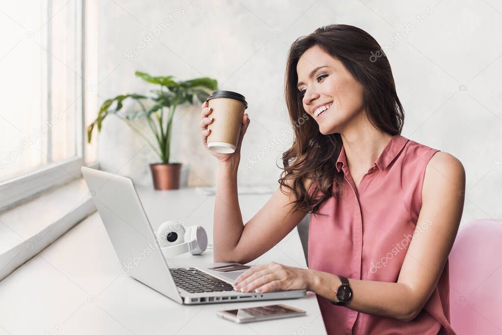 Young beautiful woman using computer while holding coffee