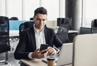 Bilgisayarda çalışan bir iş adamı. Ofiste dizüstü bilgisayar ve akıllı telefon kullanan genç bir adam. Yönetim, finans, iş kavramı