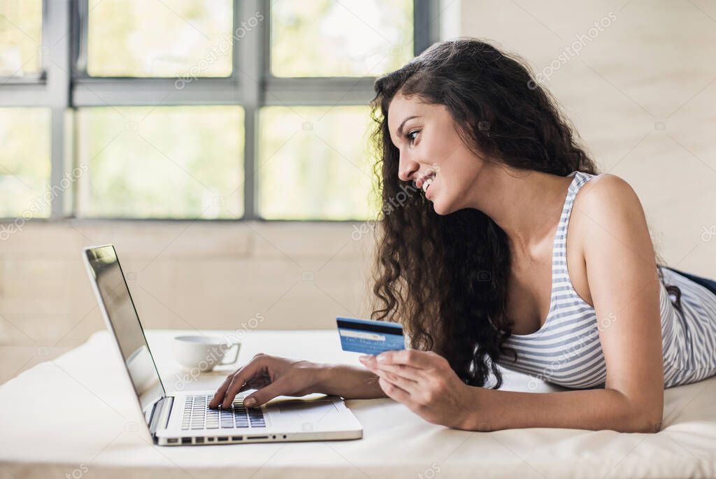 Young woman holding credit card and using laptop computer. Online shopping, enjoying life, spending money concept.