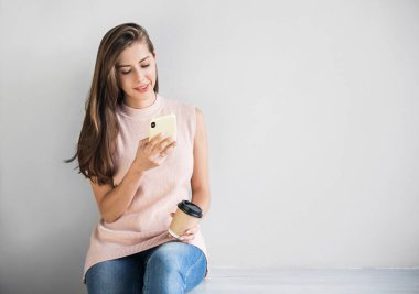 Genç, güzel, mutlu bir kadın akıllı telefon kullanıyor. Cep telefonuyla mesaj atan bir kız. Gri arkaplanda izole