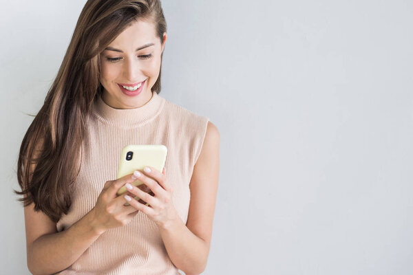 Young beautiful happy woman using smart phone. Girl texting on her mobile phone. Isolated on grey background